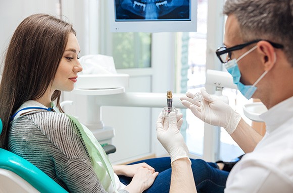 A male dentist showing his female patient a dental implant