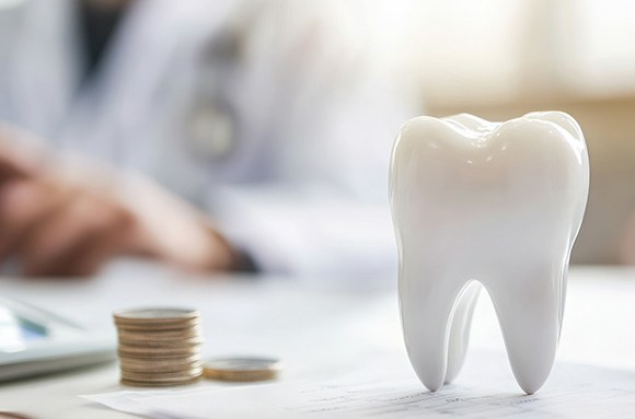 Large model tooth next to pile of coins on a desk