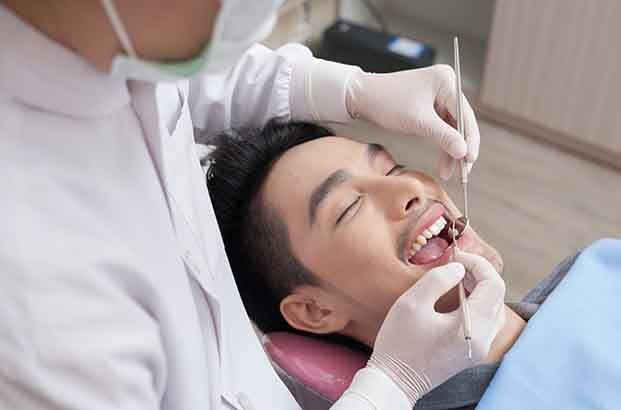 Man with black hair and eyes closed undergoing dental checkup