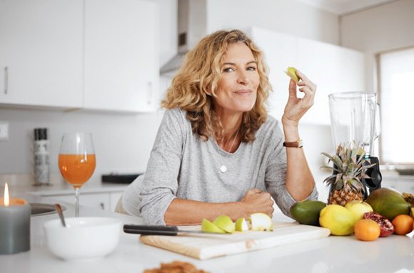 Woman smiling while eating fruit in kitchen at home