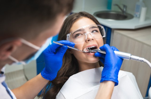 Woman with long brown hair undergoing root canal by dentist with blue gloves